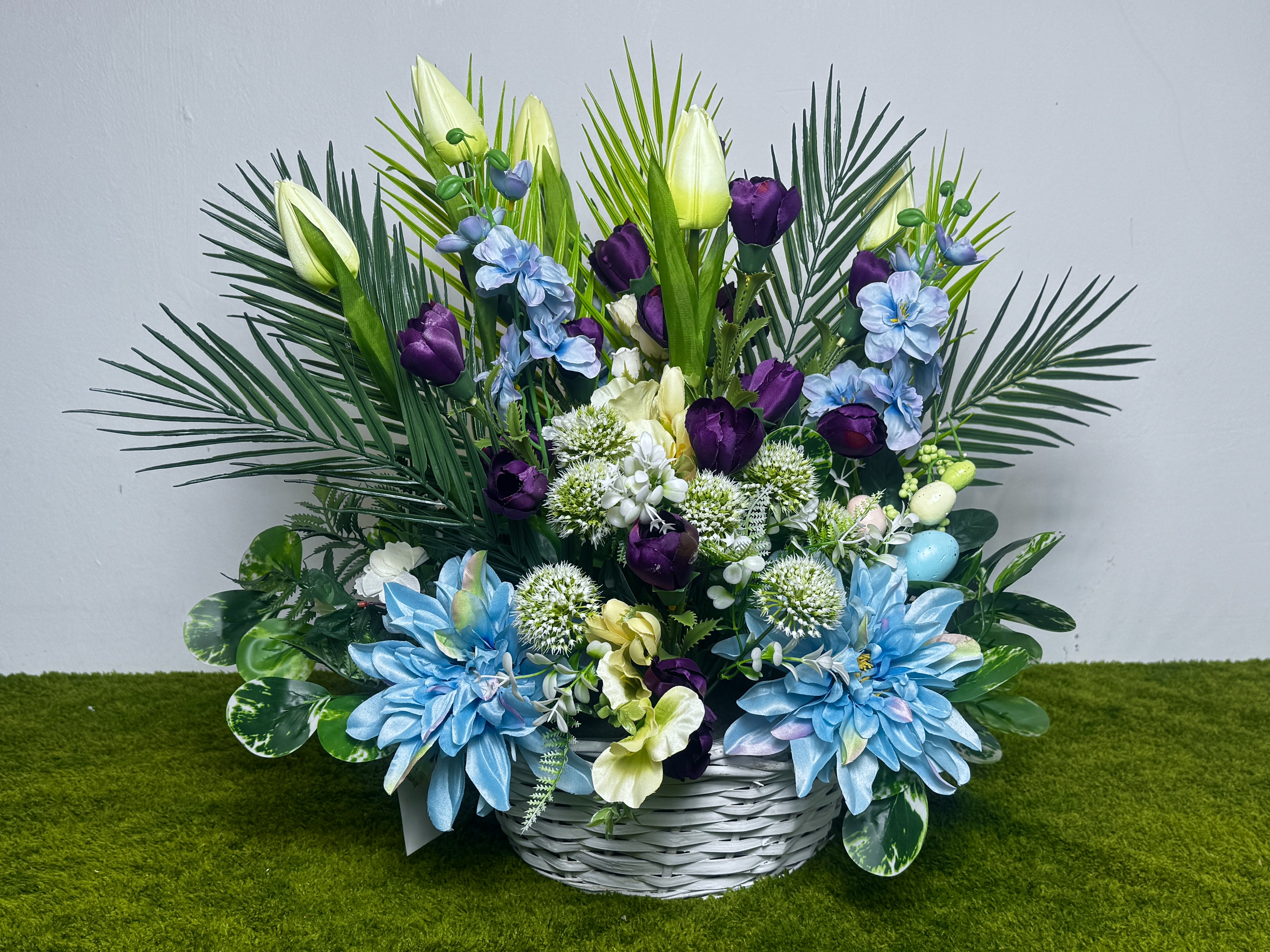 Duży wiosenny stroik w wiklinowym koszu w odcieniach niebieskiego i fioletu.