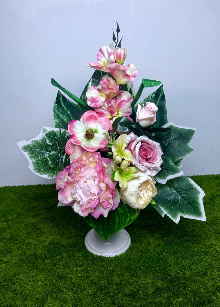 Pionowy bukiet do wazonu nagrobnego w kolorach pudrowego różu i waniliowego kremu. W składzie duże piwonie, róże i frezje. Kwiaty otoczone gęstymi zielonymi liśćmi bluszczu z białą obwódką oraz liśćmi monstery. Wysokość ok. 50 cm. Całość dociążona w czarnym wkładzie.